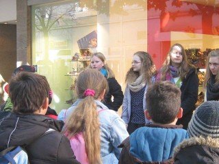 Vor einem Schuhhaus im Zentrum Mendens: Die Schülerinnen der 7b erzählen den Grundschülern, was hier zur Zeit des Nationalsozialismus geschah. (Foto: WBG/Mertens)